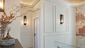 A hallway with a potted plant, a glass railing, and a door with a light fixture. - Airy Suites Athens (Athens)