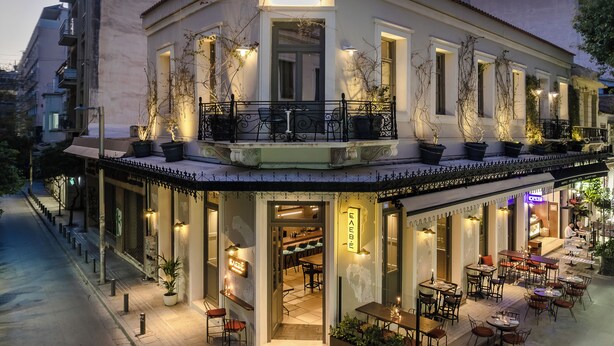 A building with a sign 'AIRY' at the entrance, outdoor seating with tables and chairs, and a balcony with potted plants. - Airy Suites Athens (Athens)