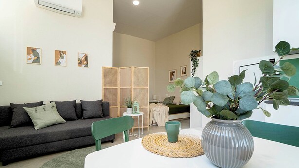 A modern living room with a dark grey sofa, a green chair, a white table with a vase of plants, and a woven placemat. - Casa del Falegname · Abete Loft with kitchen · 3 guests (Gaiana di Castel San Pietro Terme)