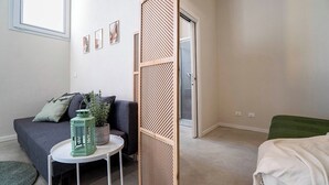 A room with a grey sofa, a small round table with a green lantern, a potted plant, and a sliding door leading to a bathroom. - Casa del Falegname · Abete Loft with kitchen · 3 guests (Gaiana di Castel San Pietro Terme)