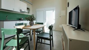 A compact kitchen with white cabinets, a dining table, and chairs. A television is mounted on the wall. - Casa del Falegname · Abete Loft with kitchen · 3 guests (Gaiana di Castel San Pietro Terme)