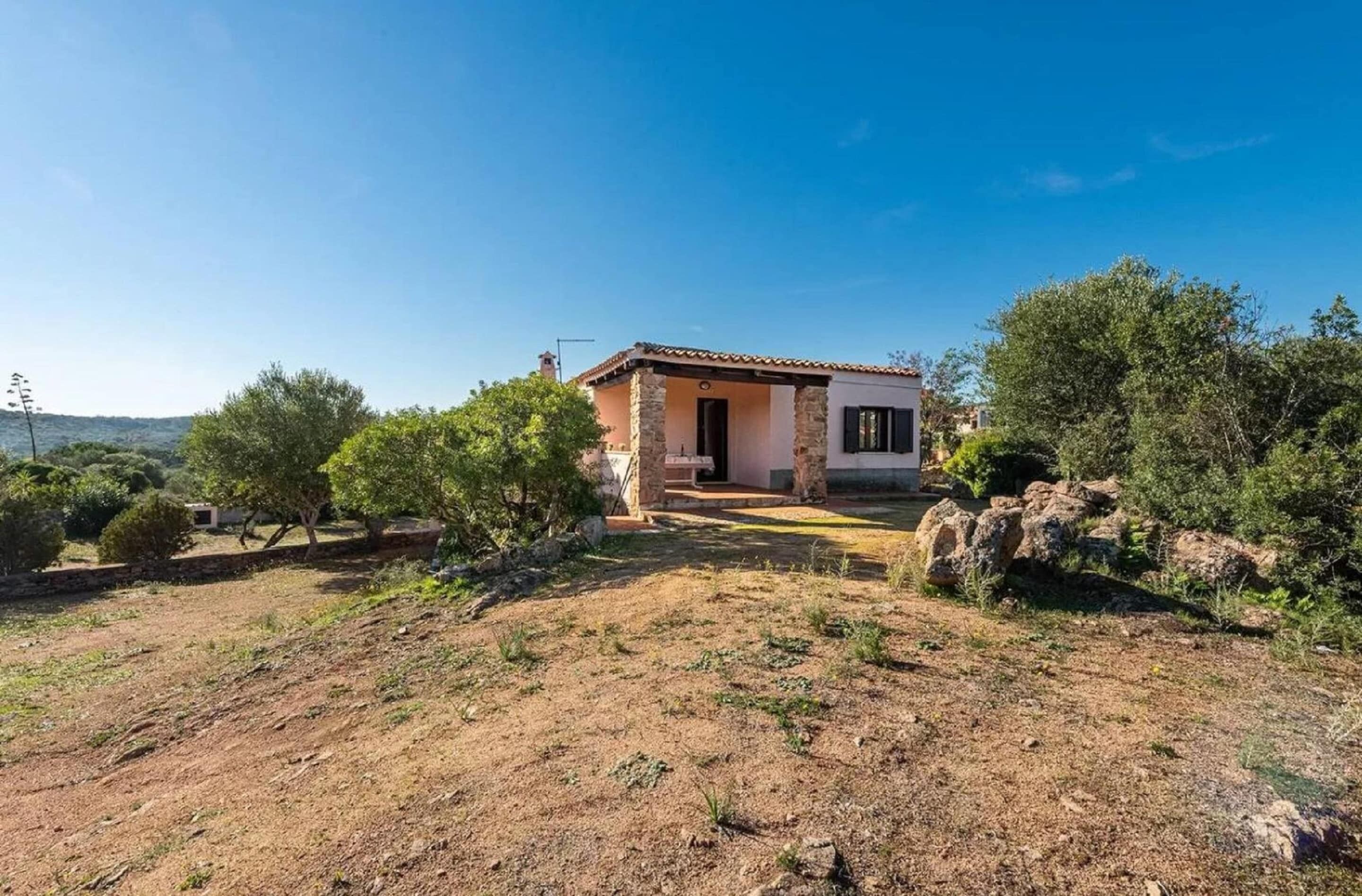 Ein eingeschossiges Haus mit Steinaußenwand und Ziegeldach, umgeben von trockenem Gras und spärlicher Vegetation.