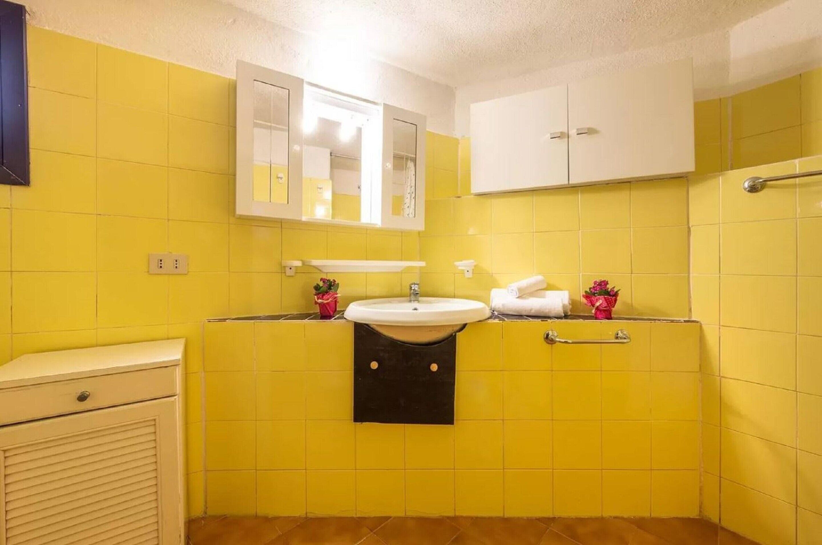 Un bany amb rajoles grogues, un lavabo blanc i un mirall a sobre.