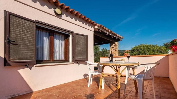 A balcony with a table and chairs, a stone pillar, and a view of greenery.