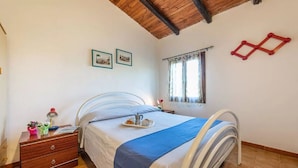 A bedroom with a bed, a nightstand, a window with curtains, and a wooden ceiling.