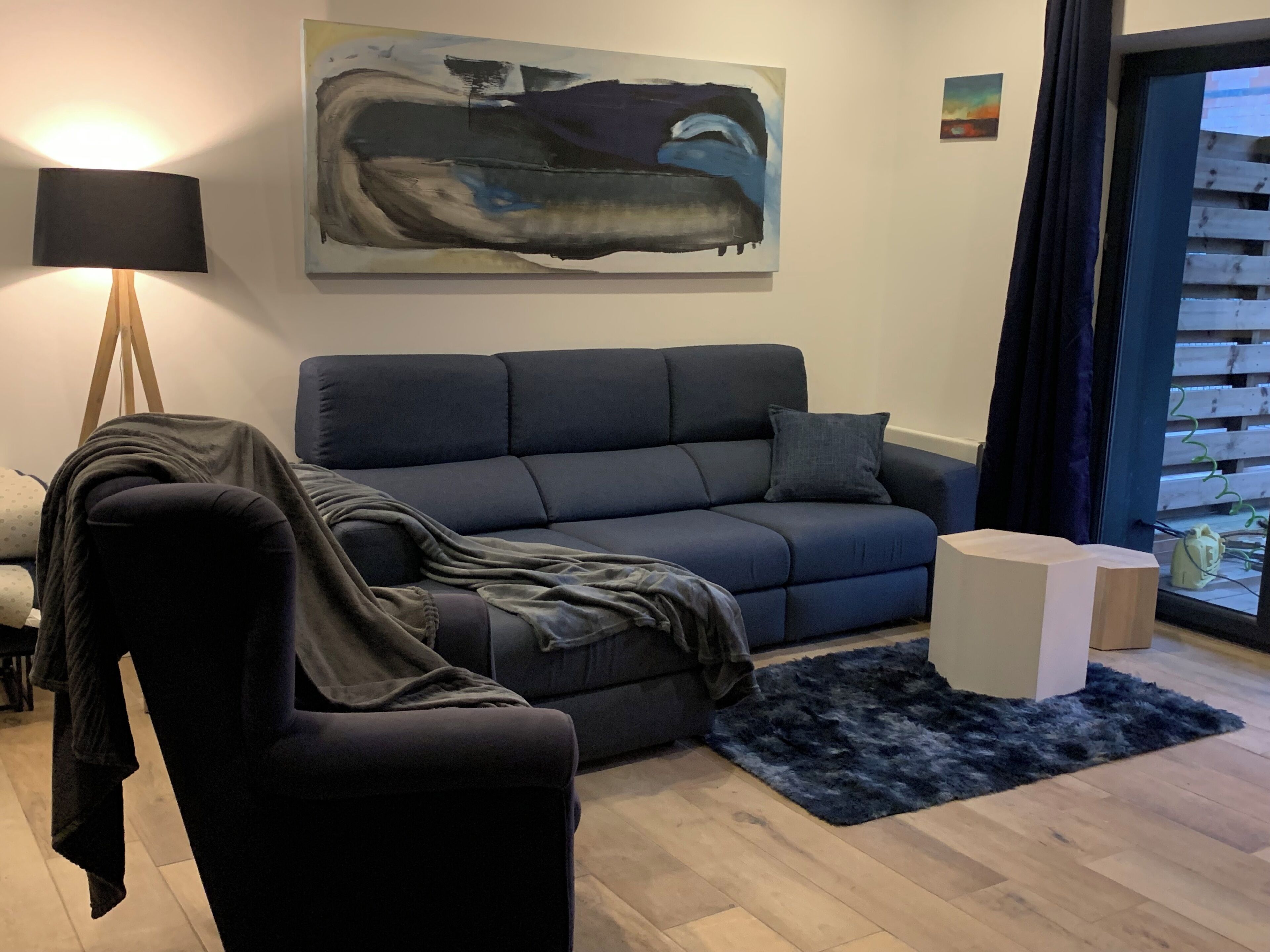 Un salon moderne avec un canapé bleu foncé, une petite table d’appoint ronde, une lampe et un tableau accroché au mur.