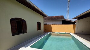 Una piscina rectangular con borde de azulejos, rodeada por un muro bajo y un edificio con techo de tejas.