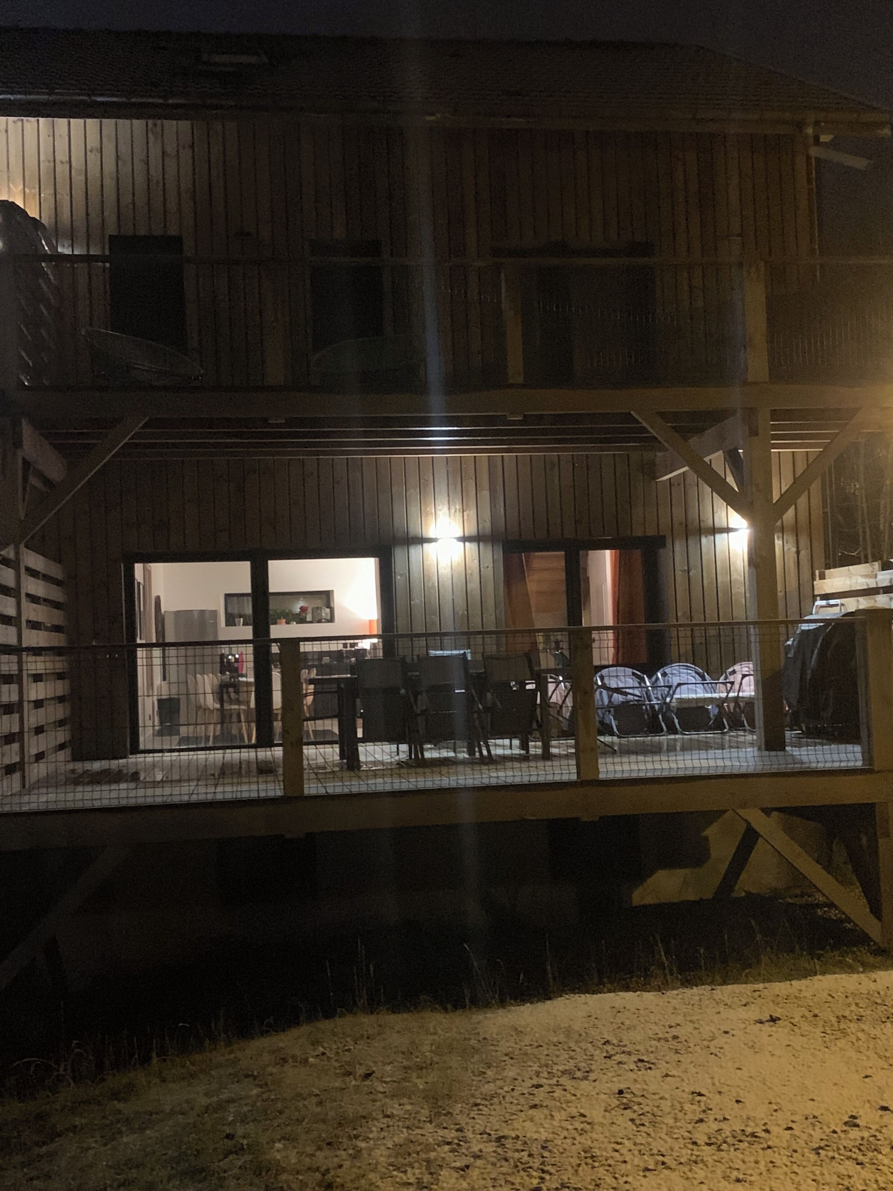 A two-story wooden building with a covered outdoor area featuring a table and chairs.