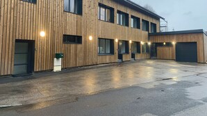 Ein modernes Gebäude mit Holzfassade, zahlreichen Fenstern und einem überdachten Parkplatz.