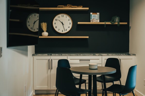 Una cucina moderna con due orologi, un tavolo da pranzo con quattro sedie e mensole con oggetti decorativi.