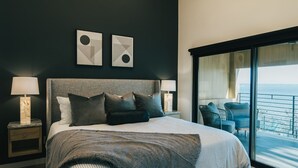 Une chambre moderne avec un grand lit, un lustre et un balcon offrant une vue dégagée.