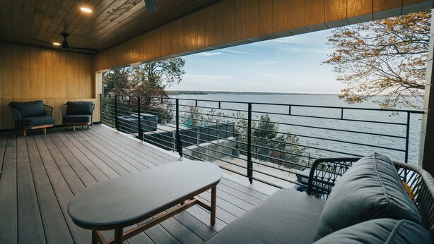 Une terrasse en bois avec une table et des chaises, un balcon avec une balustrade et une vue sur l’eau.