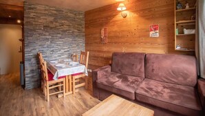 A cozy room with a wooden dining table set for two, a brown sofa, and a stone accent wall. - Floor -2, view mountain, terrace, ski locker, 30m², Valmorel (Valmorel)