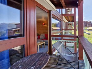 A wooden balcony with a table and chairs, a sofa, and a view of the surrounding landscape.
