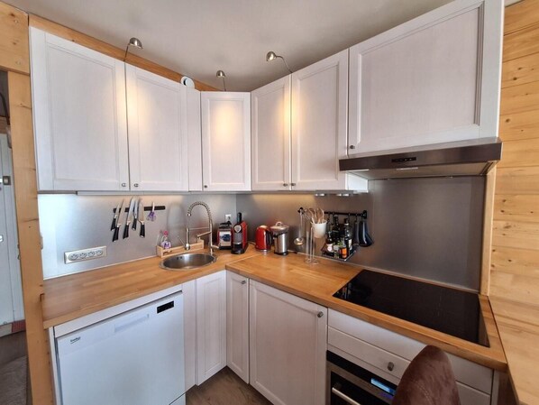 A compact kitchen with white cabinets, a wooden countertop, and stainless steel appliances including a dishwasher, a coffee maker, and a kettle.