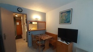 A compact room with a kitchenette, a dining table with chairs, a television on a wooden cabinet, and a framed picture on the wall. - 70m from ski slopes, 2nd floor, balcony, tv, ski locker, 19m², Valfréjus (Valfréjus)