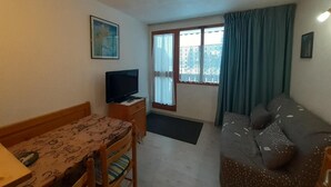 A compact room with a wooden table, a television, a sofa, and a window with curtains. - 70m from ski slopes, 2nd floor, balcony, tv, ski locker, 19m², Valfréjus (Valfréjus)