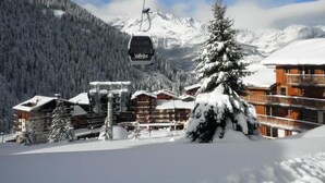A ski lift with cabins, a wooden building with balconies, and snow-covered trees. - 70m from ski slopes, 2nd floor, balcony, tv, ski locker, 19m², Valfréjus (Valfréjus)
