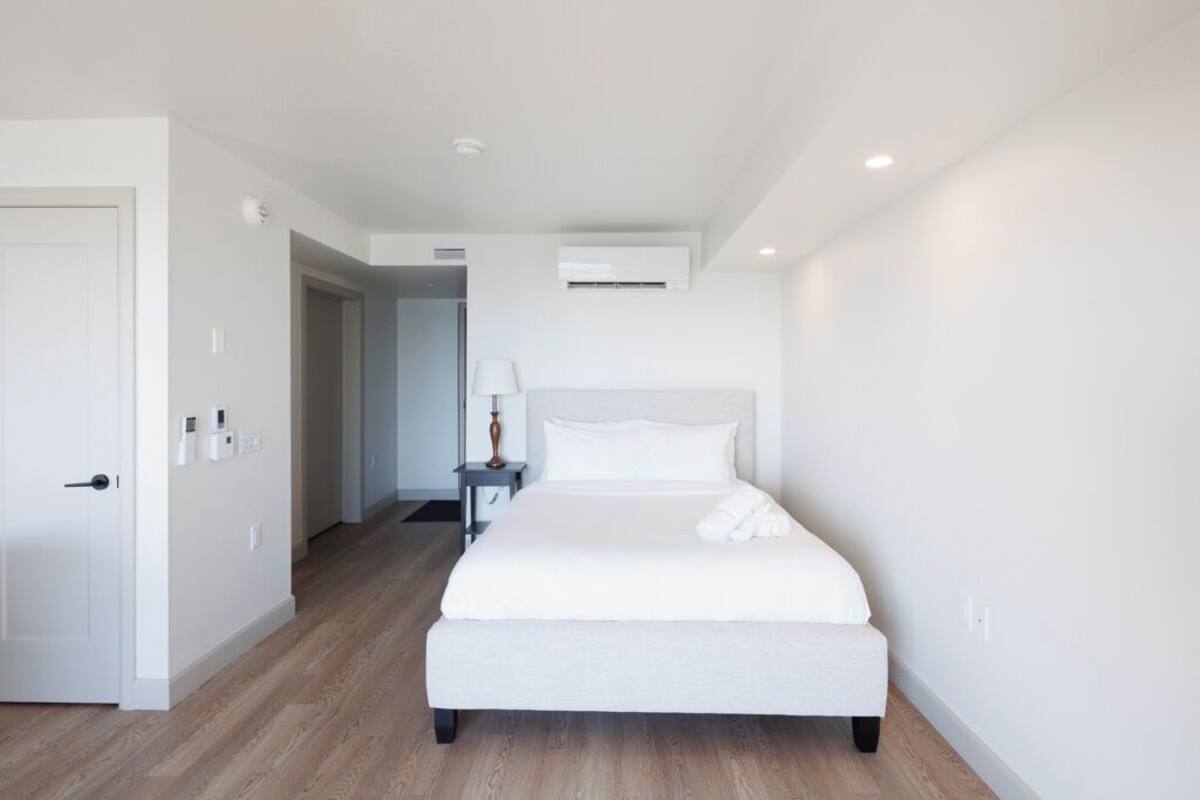 Een moderne hotelkamer met een groot bed, een nachtkastje en een wandgemonteerde airconditioning.