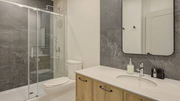 Un bagno moderno con doccia vetrata, un water bianco, parete rivestita in marmo, uno specchio grande e un mobile bagno in legno con lavabo.