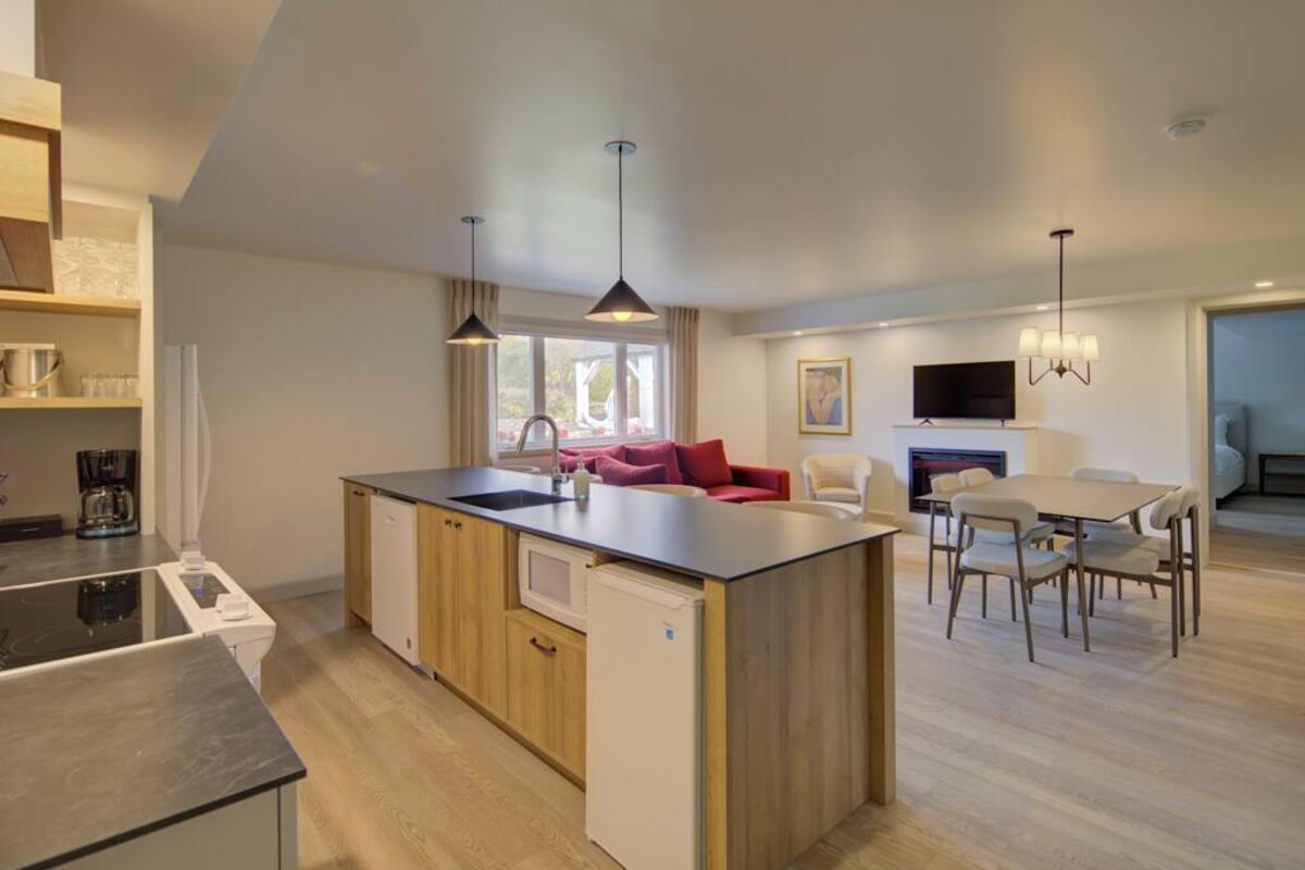 Een moderne keuken met een centraal eiland, een zithoek met een tafel en stoelen, en een woongedeelte met een bank en televisie.