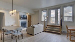 A modern living room with a sofa, dining table, and chairs, a fireplace, and large windows with a view. - La Pinsonnière (La Malbaie)