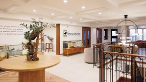 A spacious hotel lobby with a wooden reception desk, a large potted plant, and a sign for 'La Pinsonniere'. - La Pinsonnière (La Malbaie)