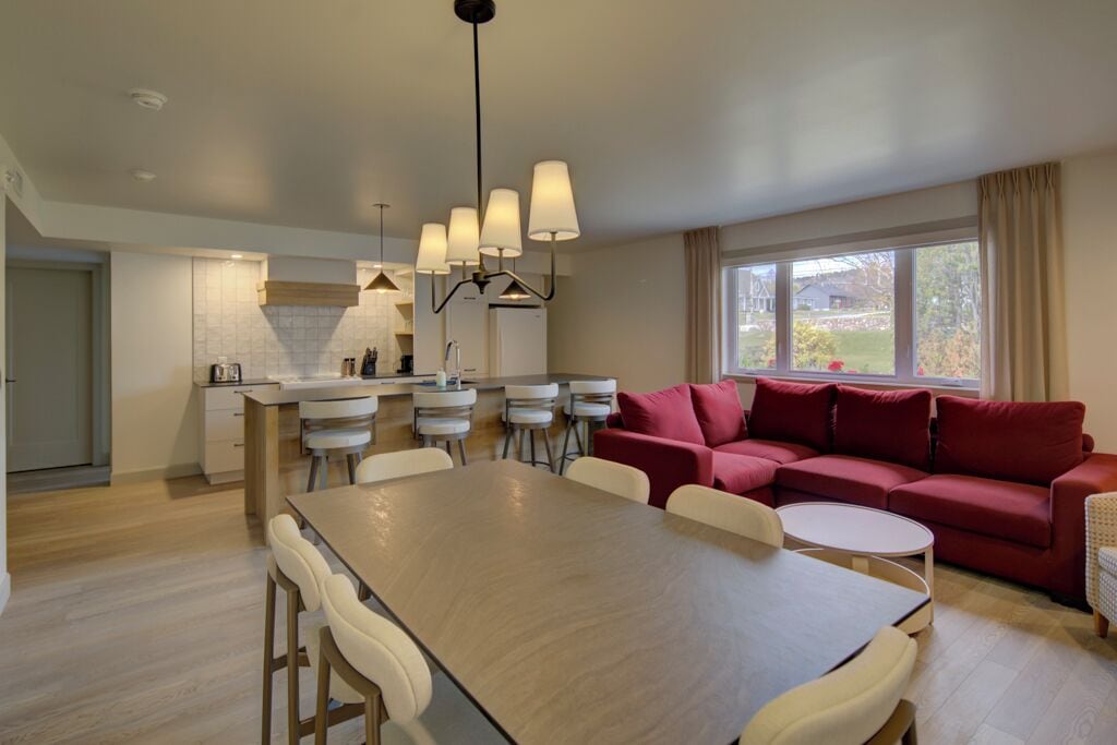 A modern living room with a dining area, a red sofa, and a kitchen in the background.