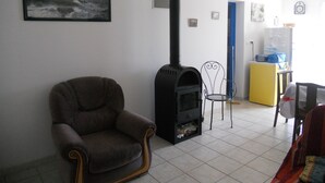 A living room with a sofa, a black stove, a chair, and a small table. - Detached house, in an enclosed garden, quiet location, near forest and sea (Saint-Vincent-sur-Jard)