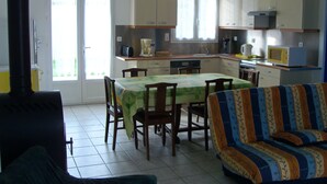 A dining area with a table and chairs, a sofa, and a kitchen with cabinets and appliances. - Detached house, in an enclosed garden, quiet location, near forest and sea (Saint-Vincent-sur-Jard)