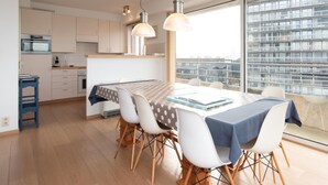 A modern kitchen with white cabinets, a dining table with a polka dot tablecloth, and a large window with a city view. - Sunny Apartment With Large Terrace (Ostend)