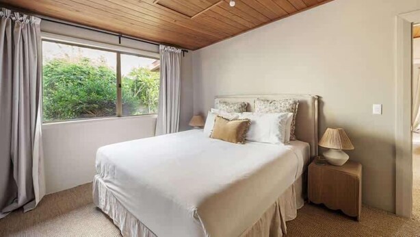 Una camera da letto con un letto grande, una finestra con tende, un comodino con una lampada e un soffitto in legno.