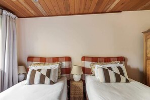 A room with two beds, wooden headboards, bedside lamps, and a wooden ceiling.