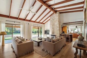 A spacious living room with a stone fireplace, wooden beams, and a large window overlooking a garden. - Orchard Homestead—A True Rural Wellness Escape (Yallingup Siding)