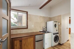 A compact kitchen with a built-in washer and dryer, wooden cabinets, a window, and a door leading to another room.