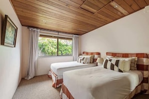 Une chambre avec deux lits, un plafond en bois, une fenêtre avec des rideaux et un tableau encadré au mur.