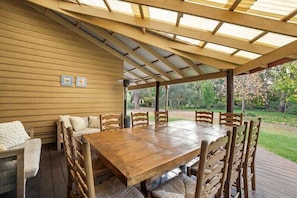 Ein überdachter Essbereich im Freien mit einem Holztisch und -stühlen, einer Pergola darüber und Blick auf einen Garten.