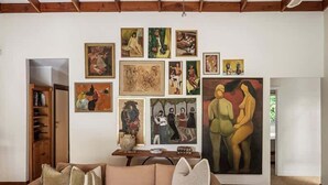 Un soggiorno con un divano beige, un tavolino da caffè e una parete decorata con diverse opere d'arte.