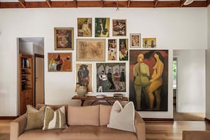 Un salon avec un canapé beige, une table basse et un mur orné de diverses œuvres d’art.