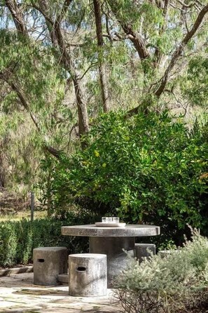 Una mesa de piedra con cuatro taburetes en un entorno natural, con árboles y arbustos.