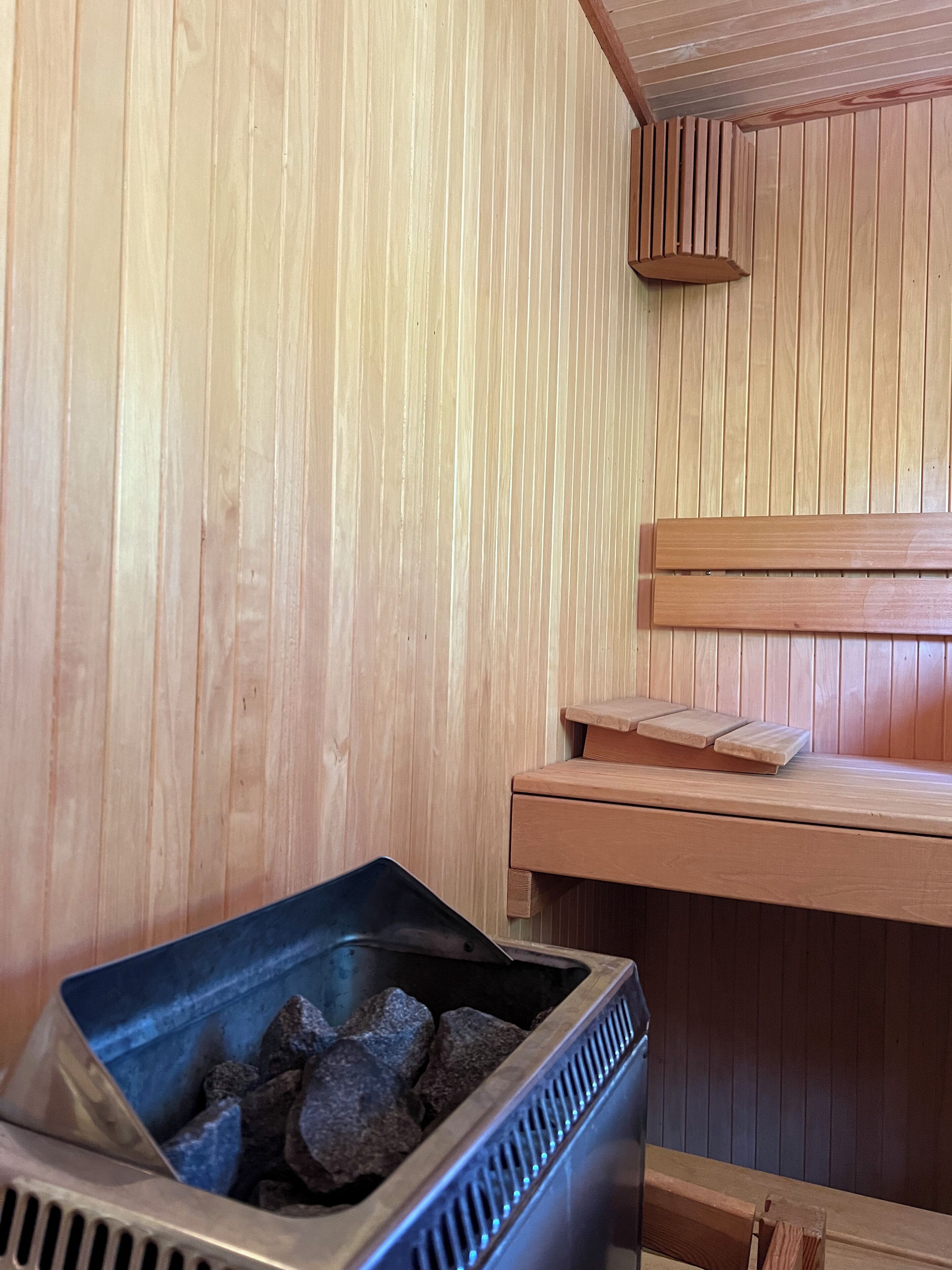 A sauna room with wooden walls, a bench, and a metal container with rocks.