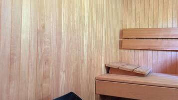 A sauna room with wooden walls, a bench, and a metal container with rocks.