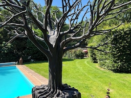 Una escultura de árbol en un jardín con piscina y césped.