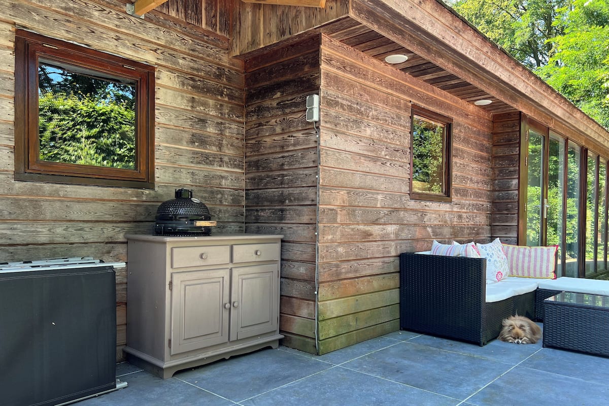 Une cabane en bois comprenant un coin repas, un barbecue et une grande fenêtre donnant sur un paysage verdoyant.