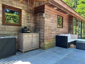 A wooden cabin with a dining area, a grill, and a large window overlooking greenery. - villa de nachtegaal (Naarden)