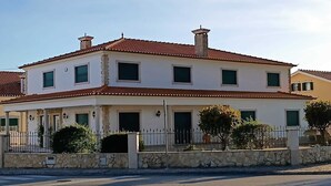 A two-story house with a red-tiled roof, a stone wall, and a metal fence. - Stunning Town Villa close to beach and Golf courses (Caldas da Rainha)