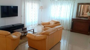 A living room with a sofa set, a flat-screen TV, and a lamp. - Stunning Town Villa close to beach and Golf courses (Caldas da Rainha)