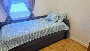 Une petite pièce agréable, avec un lit, une fenêtre avec des rideaux et un plancher en bois.