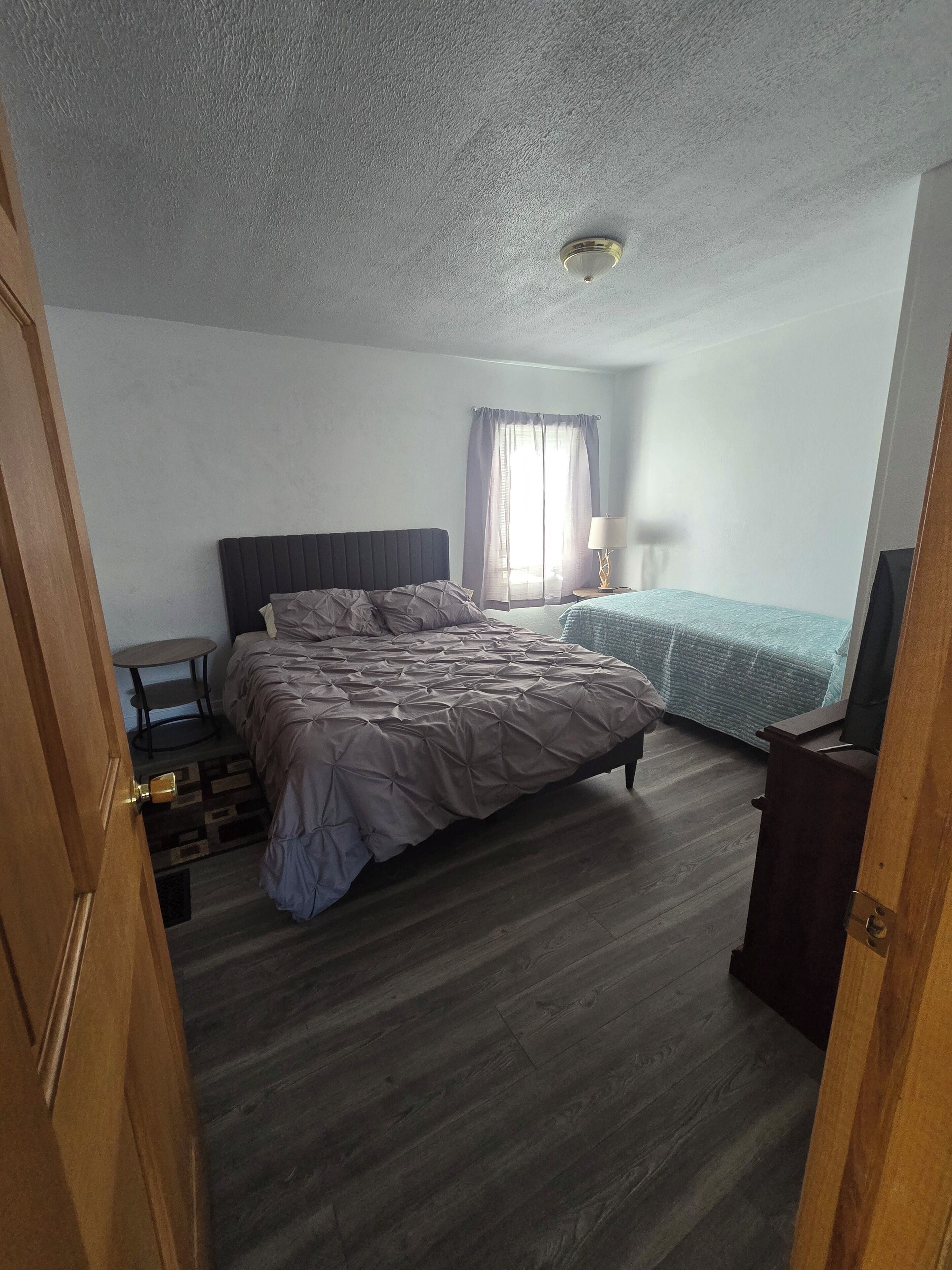 Une chambre à coucher avec un lit, une table de chevet, une lampe et une fenêtre avec des rideaux.