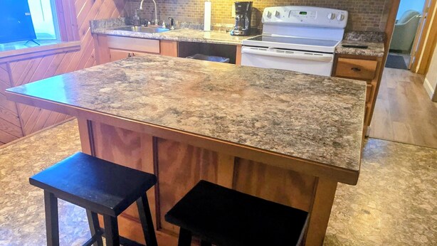 Une cuisine avec des meubles en bois, un plan de travail en granit, une cuisinière blanche, un four à micro-ondes et deux tabourets de bar.